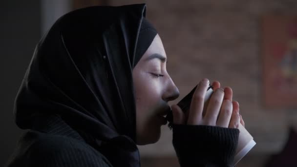 Mujer musulmana joven en hiyab Tomando té o café y mirando hacia otro lado pensando en resolver el problema, la búsqueda de la mujer seria de inspiración hacer que la decisión se siente falta de ideas, de cerca — Vídeos de Stock