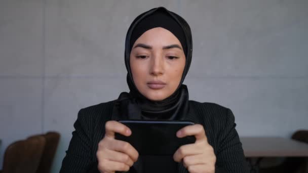 Joyful Young Muslim woman in hijab is playing video game in smartphone. Gadgets concept. Concept of technology, gaming app, online life and Metaverse. Traditional Islamic culture and religion concept — Stock Video