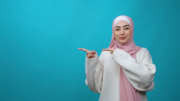 Páni, podívejte se na šílenou reklamu. Překvapen Mladá muslimka v hidžábu otevřených úst v úžasu a ukazující kopírovací prostor, ukazuje prázdnou stěnu pro váš propagační text. izolované uvnitř — Stock video