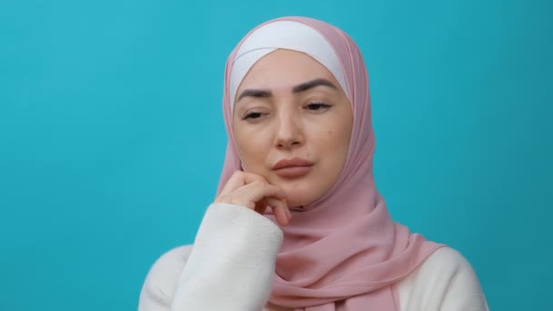 Jeune femme musulmane réfléchie dans le hijab se frottant le menton et regardant de côté avec une expression coûteuse. réfléchir à une solution, douter de la question. studio intérieur tourné isolé — Video