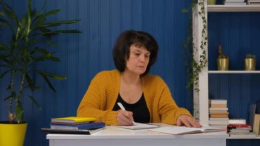Orta yaşlı bir kadın evde ders çalışıyor. Eğitim ve öğrenim kavramı