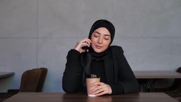 Young Muslim woman in hijab talking on the phone whit coffee. Family or business Call. Concept of online conversation and communication. Traditional Islamic culture and religion concept. — Stock Video