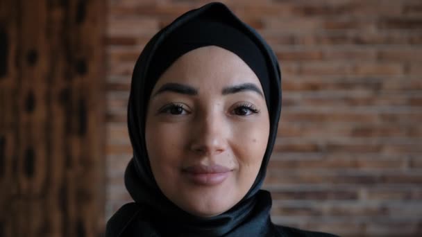 Une vue rapprochée d'une femme arabe heureuse portant un hijab noir sourit à la caméra debout. Culture islamique traditionnelle et concept de religion. — Video