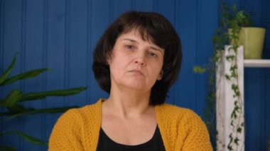 Orta yaşlı güzel bir kadın evde yalnız başına kameraya bakıyor. Oturma odasındaki manzara portresini kapat