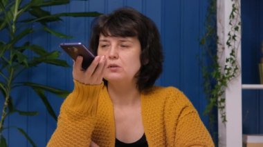 Elinde telefon tutan orta yaşlı bir kadın akıllı telefondan sanal dijital ses asistanı aktifleştiriyor. Evinden, kolay internet servisinden, ai akıllı teknoloji yardımından arama yapmasını istiyor.