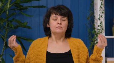 Orta yaşlı kadın meditasyonu ve evde nilüfer çiçeği pozu vererek rahatlama. Denge kavramı, uyum, zihinsel uygulama.