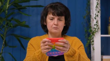 Orta yaşlı bir kadın stres önleyici silikon oyuncak kullanıyor. Stres kavramı, rahatlama, endişe. Renkli oyuncak eğilimi