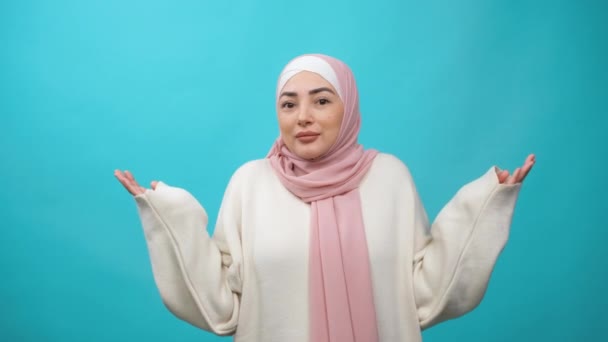 Vet inte, vem bryr sig. Glad härlig Ung Muselman kvinna i hijab rycka axlar, ser med osäker clueless uttryck, demonstrera likgiltighet tvivel. inomhus studio skott isolerad — Stockvideo