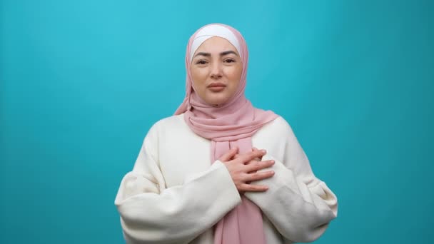 Szívproblémák. Fiatal muszlim nő hidzsáb szorító mellkasban, heveny fájdalmat érez, szívroham szorongás miatt, infarktus tünet. beltéri stúdió lövés elszigetelt kék háttér — Stock videók
