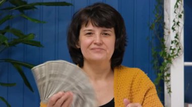 Dolar banknotları sallayan orta yaşlı bir kadın. Amerikan parası kadınların elinde. Başarılı insanlar piyango kazanır. Tasarruf, banka yatırımı, kar tüccarı kavramı
