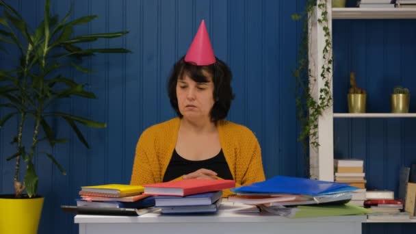 Trieste eenzame zakenvrouw die alleen op het werk zit met een verjaardagshoed en alleen haar verjaardag viert. Droevige vrouw van middelbare leeftijd — Stockvideo