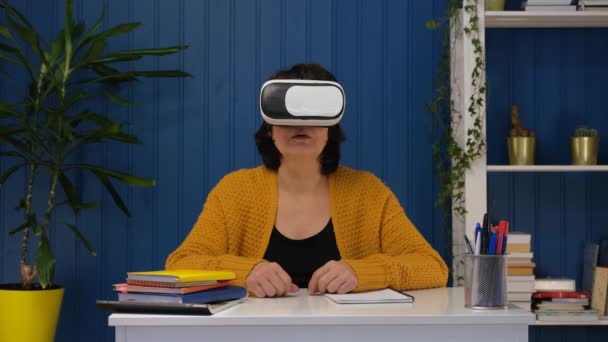 Mulher de meia idade na sala de estar usando óculos de realidade virtual. Educação on-line e metaverso em casa usando tecnologias modernas VR AR do futuro. — Vídeo de Stock