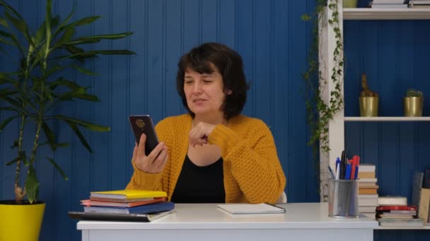 Mujer de mediana edad hablando en videollamada usando teléfono móvil en casa. — Vídeos de Stock