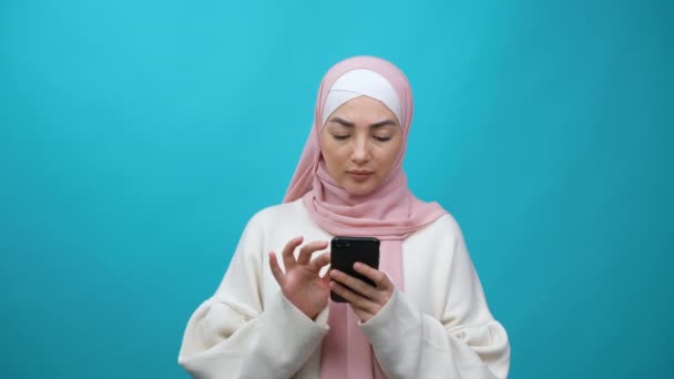 Fiatal muzulmán nő hidzsábban online vásárol mobiltelefonon hitelkártyával. Üzletelési koncepció, banki alkalmazás támogatás, e-business, biztonsági finanszírozás. Elszigetelt stúdió lövés a kék háttér — Stock videók