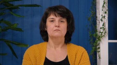 Evinde kameraya bakan orta yaşlı bir kadın.