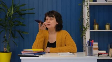 Elinde telefon tutan orta yaşlı kadın akıllı telefondan sanal dijital ses asistanını, kolay internet servisini, ai akıllı teknoloji yardımını etkinleştirdi.