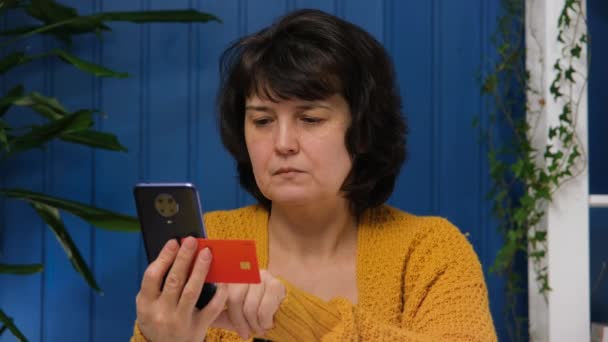 Kobieta w średnim wieku używa telefonu komórkowego do zakupów online i posiadania karty kredytowej w domu — Wideo stockowe