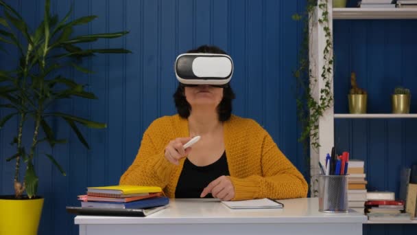 Keski-ikäinen nainen yllään vr suojalasit 3d visualisointi ja tutkia metaverse futuristinen elämäntapa. Online koulutus kotona käyttäen VR AR modernin teknologian tulevaisuuden. — kuvapankkivideo