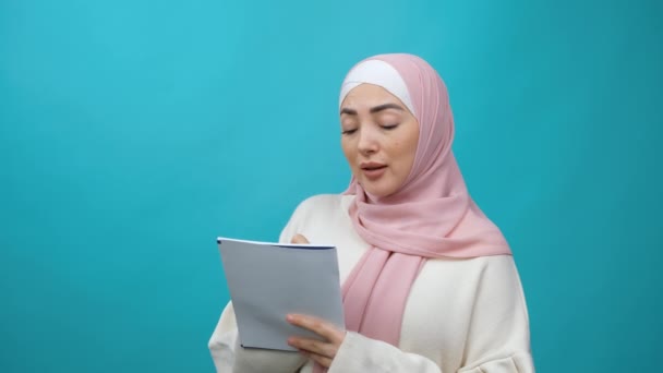 Pensativo creativo Joven musulmana en hijab pensando en el futuro plan de negocios, tomando notas en cuaderno de papel, escribiendo idea creativa y sonriendo inspirado feliz. Grabación de estudio aislada — Vídeo de stock