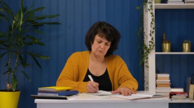 Orta yaşlı bir kadın evde ders çalışıyor. Eğitim kavramı