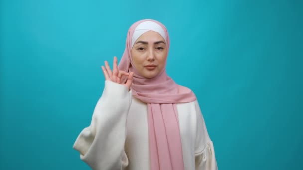 Mujer musulmana joven en hijab Mira la cámara con aprobación decir wow está bien mostrando gesto signo bien. Grabación de estudio aislada — Vídeos de Stock
