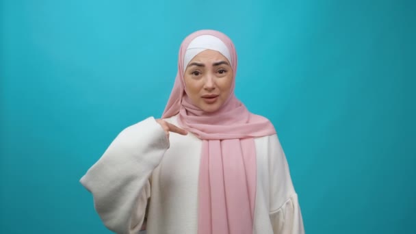 Молодая мусульманка в хиджабе смотрит в камеру указывая пальцами себя спросить, кто я нет, спасибо мне не нужно это Изолированная студия съемки — стоковое видео