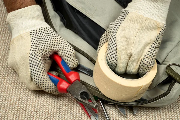 Bir adamın elleri pense ve koli bandıyla, artı diğer aletlerle.