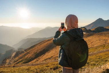 Adamın biri, dağın tepesindeki muhteşem manzaranın akıllı telefonuyla fotoğraflarını çekiyor.