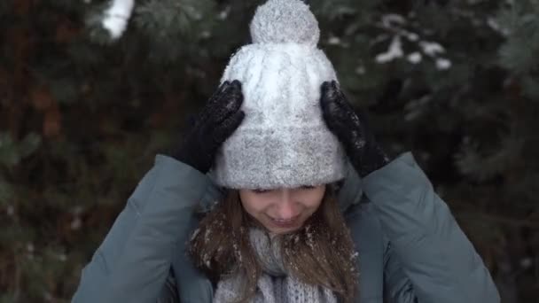 Een mooi meisje schudt de sneeuw van haar grijze hoed. Close-up. — Stockvideo