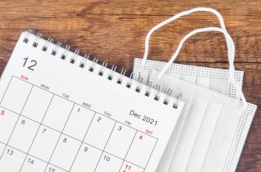 Aralık 2021. Masa takvimi, ahşap arka planda cerrahi maske takılı..