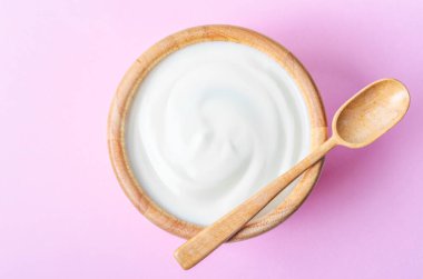 Pembe arka planda ahşap bir kasede tahta kaşıkla Yunan yoğurdu.