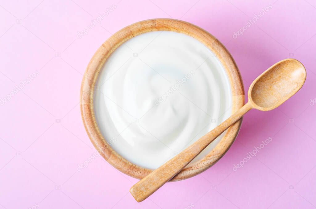Greek yogurt with wooden spoon in a wooden bowl on pink background.