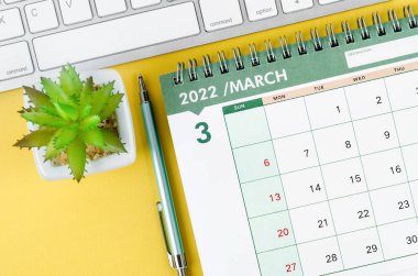 Sarı arkaplanda klavye bilgisayarlı Mart 2022 masa takvimi ve günlük.
