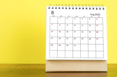 Ahşap masanın üzerinde sarı arkaplan olan Ağustos 2022 masa takvimi..