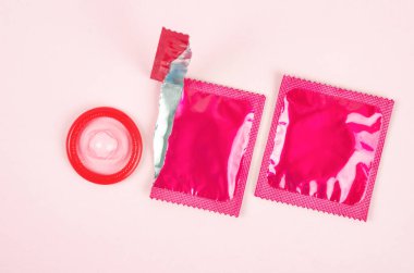 Pembe arkaplanda açık prezervatif paketi var. Güvenli seks ve üreme sağlığı kavramı.