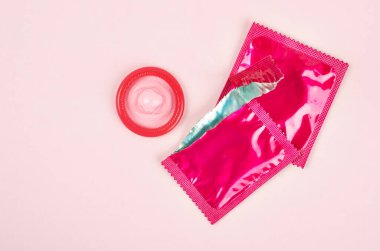 Pembe arkaplanda açık prezervatif paketi var. Güvenli seks ve üreme sağlığı kavramı.