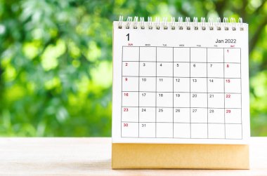 Doğanın arka planındaki ahşap masa üzerinde organizatörün planlaması ve hatırlatması için Ocak 2022 takvim masası.