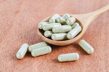 Ahşap arka planda kapsüllerde bitkisel ilaç yığını.