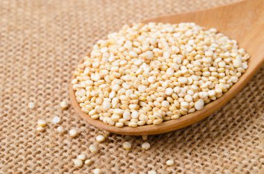 Çiğ, bütün, işlenmemiş kinoa tohumu tahta kaşıkta, arka planda.