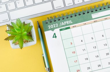 THe Arpil 2022 desk calendar and diary with keyboard computer on yellow background.