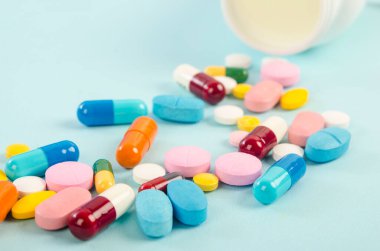 İlaç hapları ve haplar mavi arka planda bir ilaç şişesinden dökülüyor.