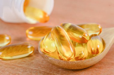 Tahta arka planda kaşık üzerinde morina yağı Omega 3 jel kapsülleri. Balık yağı vitaminleri.