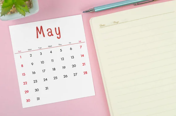 The May 2022 calendar with note book on pink background.