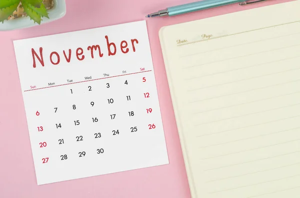 The November 2022 calendar with note book on pink background.