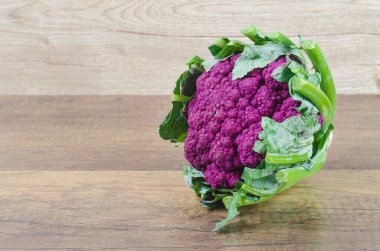 Tahta arka planda yeşil yaprakları olan taze Karnabahar moru. Vejetaryen yemeği..