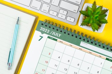 Sarı arkaplanda klavye bilgisayarlı Temmuz 2022 masa takvimi ve günlük.