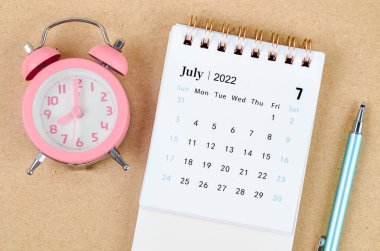 Kahverengi zemin üzerinde pembe alarm saati bulunan Temmuz 2022 Masa takvimi.