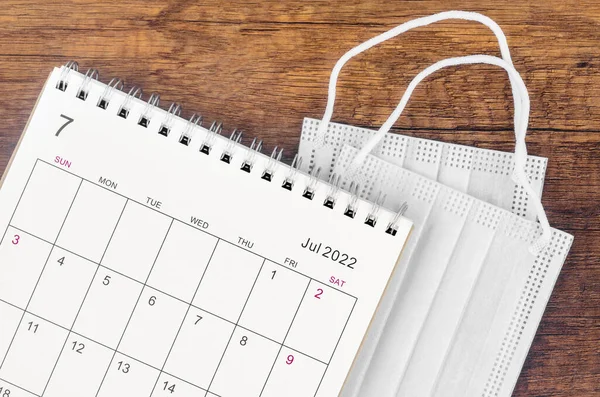 Tahta arka planda cerrahi maske takılı Temmuz 2022 masa takvimi.