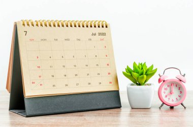 Ahşap masa üzerinde pembe alarm saati olan Temmuz 2022 Masa takvimi..