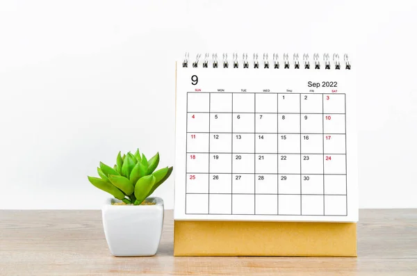 The September 2022 desk calendar with plant on wooden table.